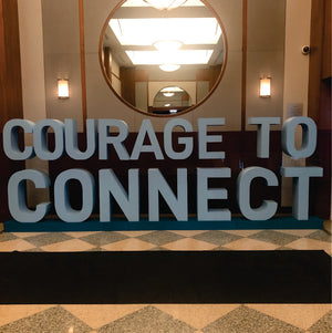 Large foam letters in bold silver-grey spell out 'COURAGE TO CONNECT,' displayed indoors. Ideal for events and branding